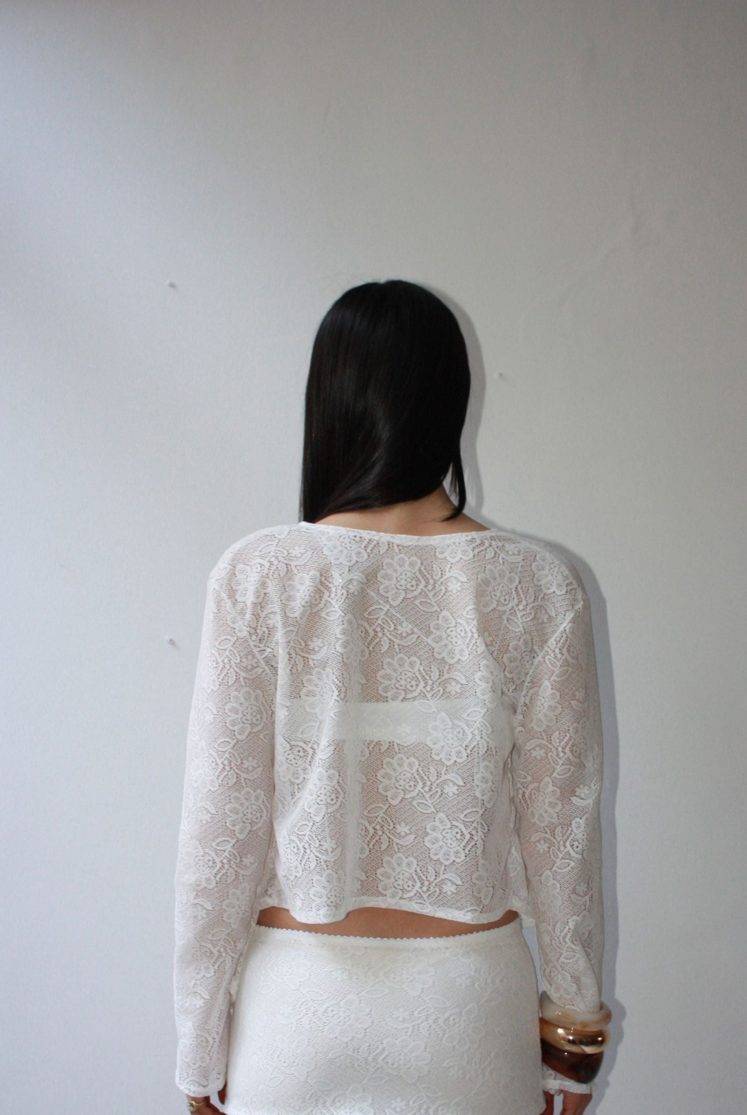 Back view of a woman wearing a white lace cardigan with floral patterning.