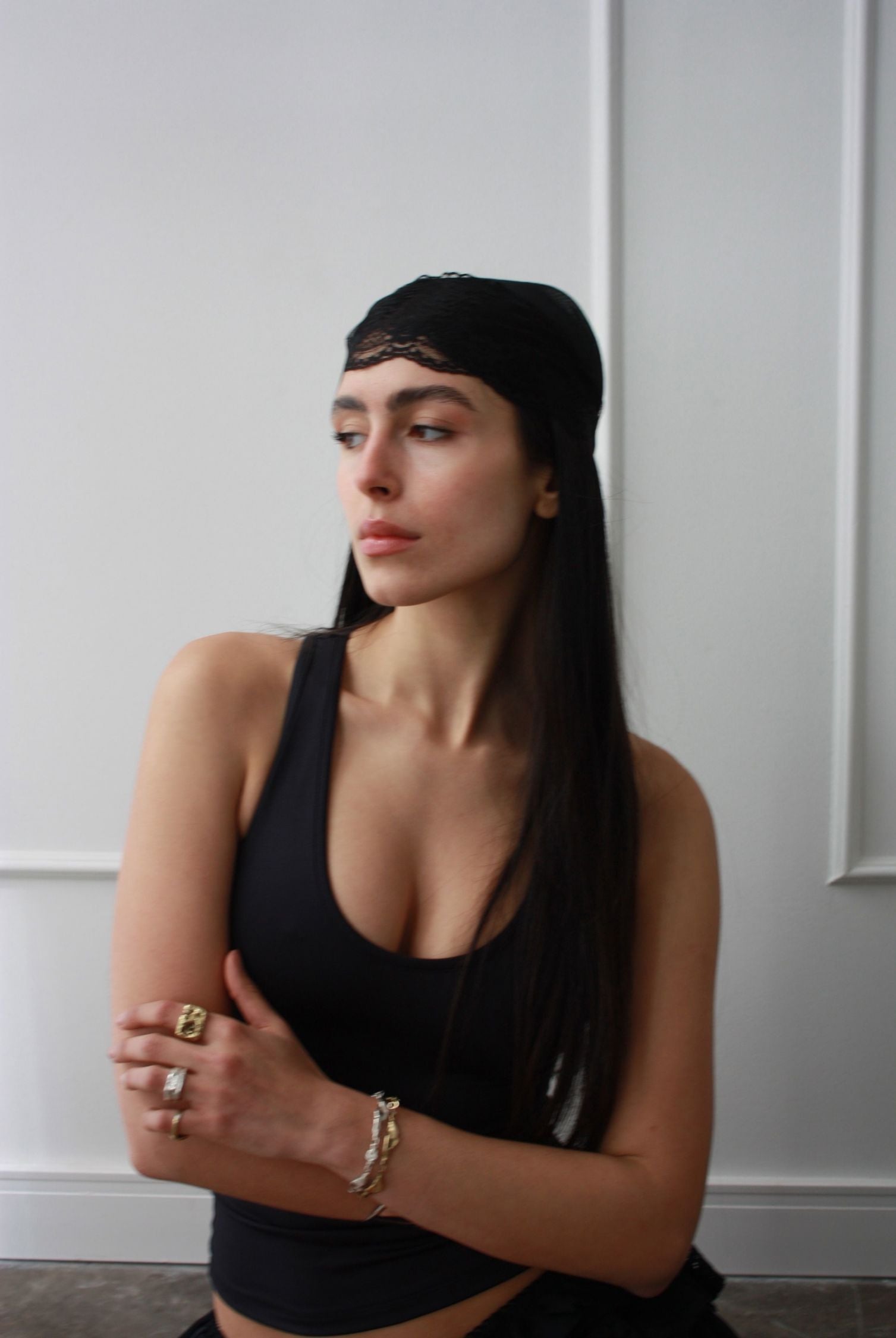 A black boho chic antique style bandana tied around a woman's head. Her arms are crossed and she looks off into the distance.