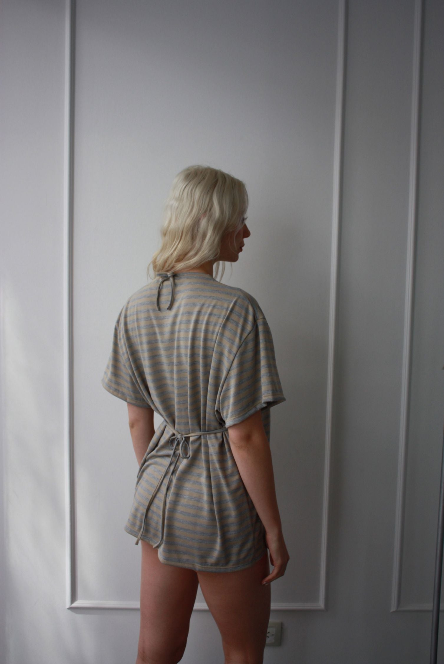 Model standing shows the back of a blue and white striped oversized t shirt that has been cinched at the waist to create an hourglass figure.