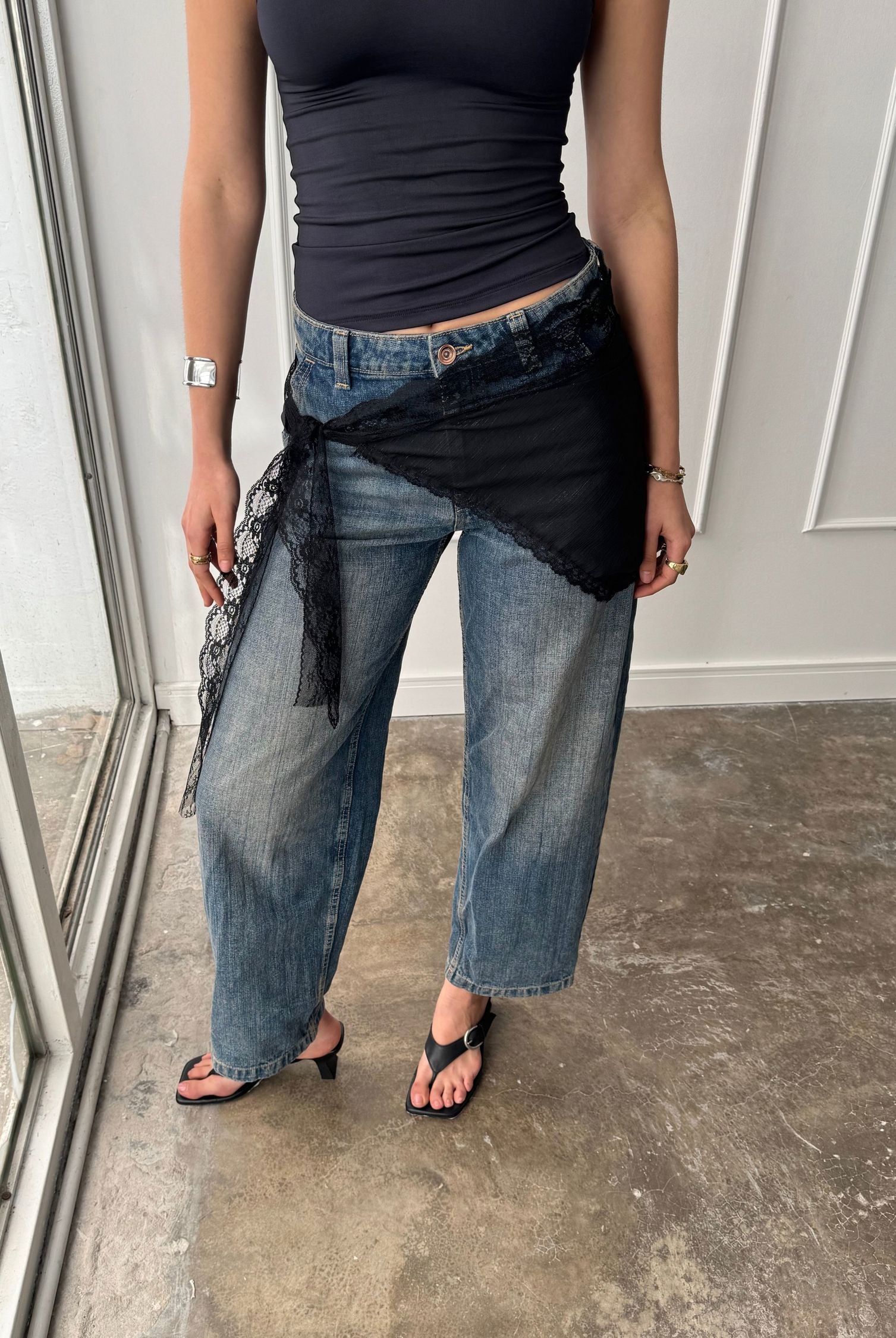 Woman standing with a black lace bandana tied around her waist. Its delicate floral patterning highlights an effortless feminine Boho chic air.