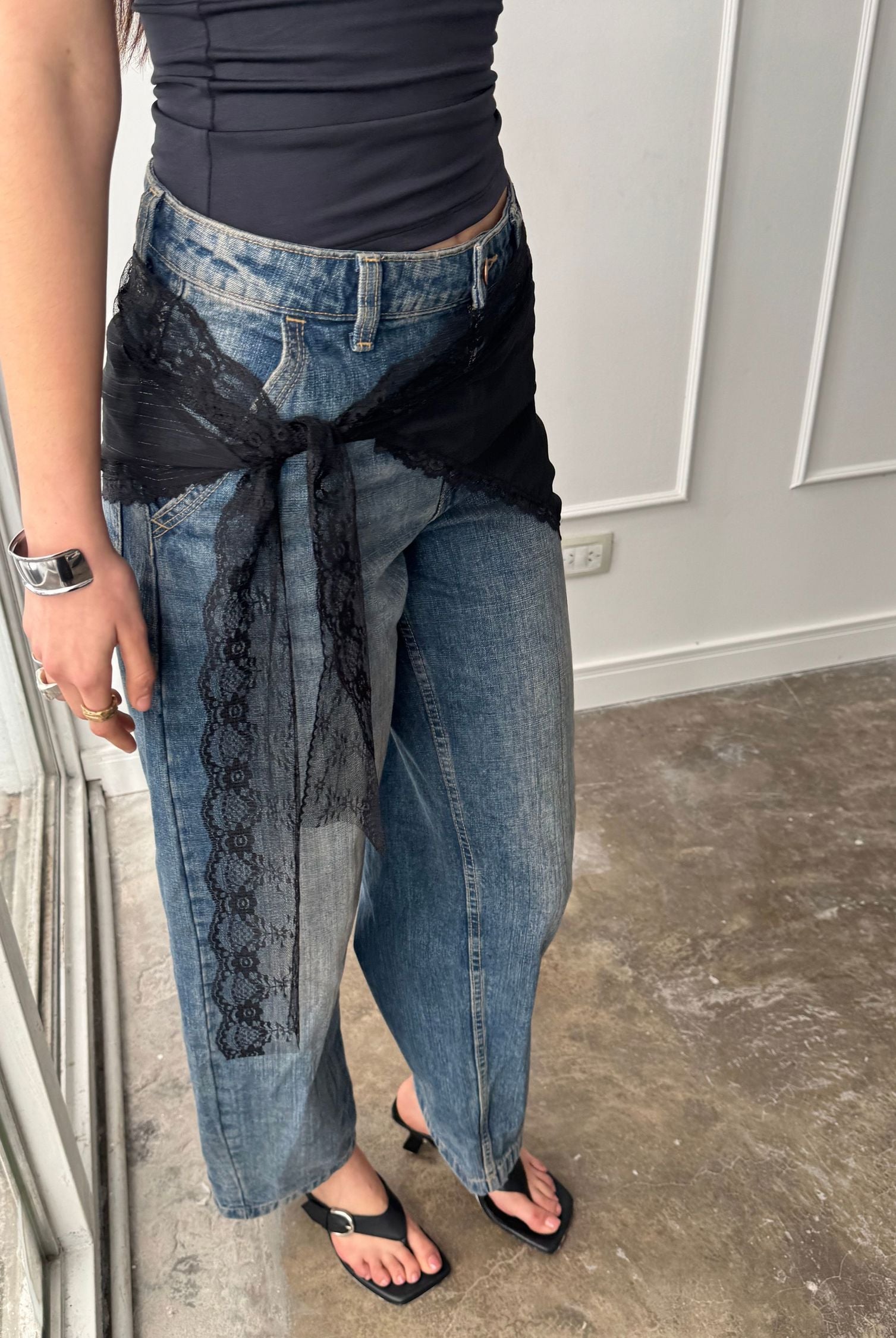 A black lace bandana tied around the waist. Its delicate floral patterning and bohemian air elevates a black top paired with baggy jeans.
