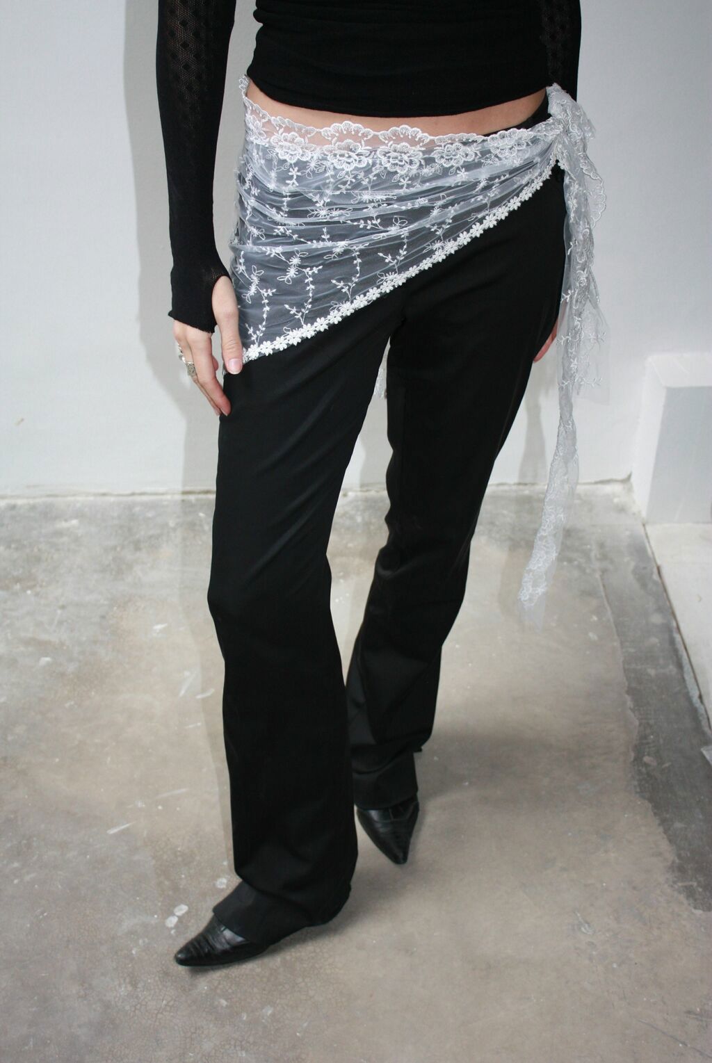 A model wears a delicate white lace bandana with floral applique motifs tied around her hips.